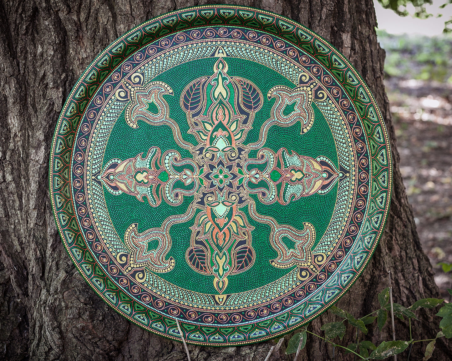 Round metal serving tray for ottoman, from Fantasy Forest collection, made in green and gold. Front view outdoor on the wooden background.