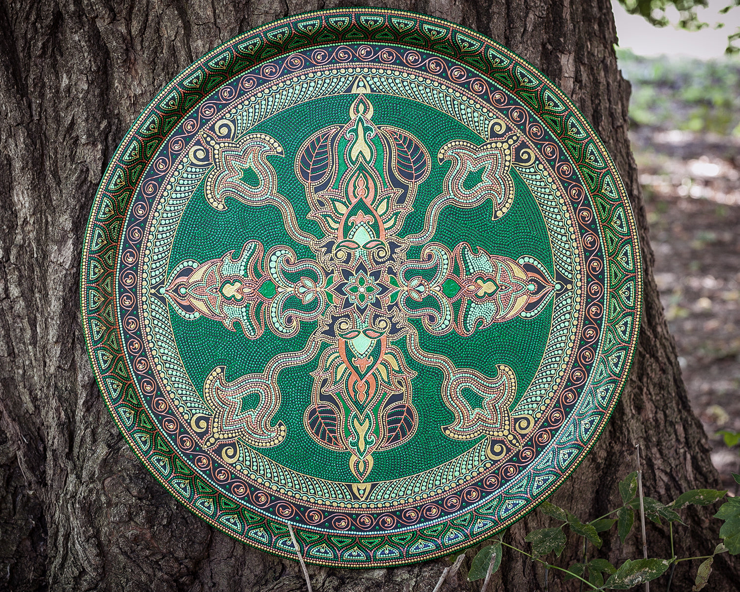 Round metal serving tray for ottoman, from Fantasy Forest collection, made in green and gold. Front view outdoor on the wooden background.