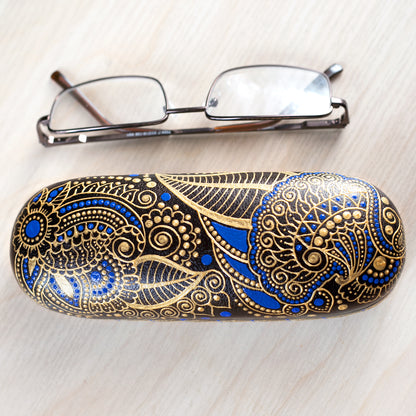 Hardshell case for glasses, hand-painted with blue and gold mehndi design. View from the top, reading glasses are on the side to show dimensions of the case.