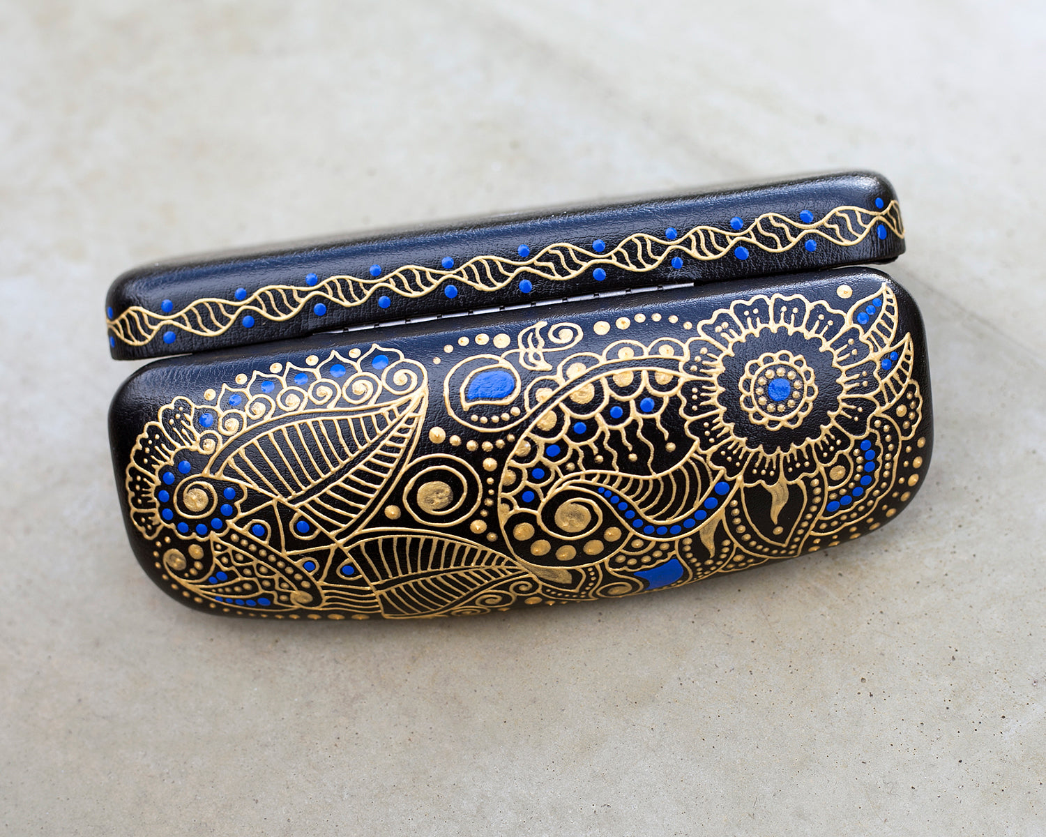 Hardshell case for glasses, hand-painted with blue and gold mehndi design. View from the top, the case is open.