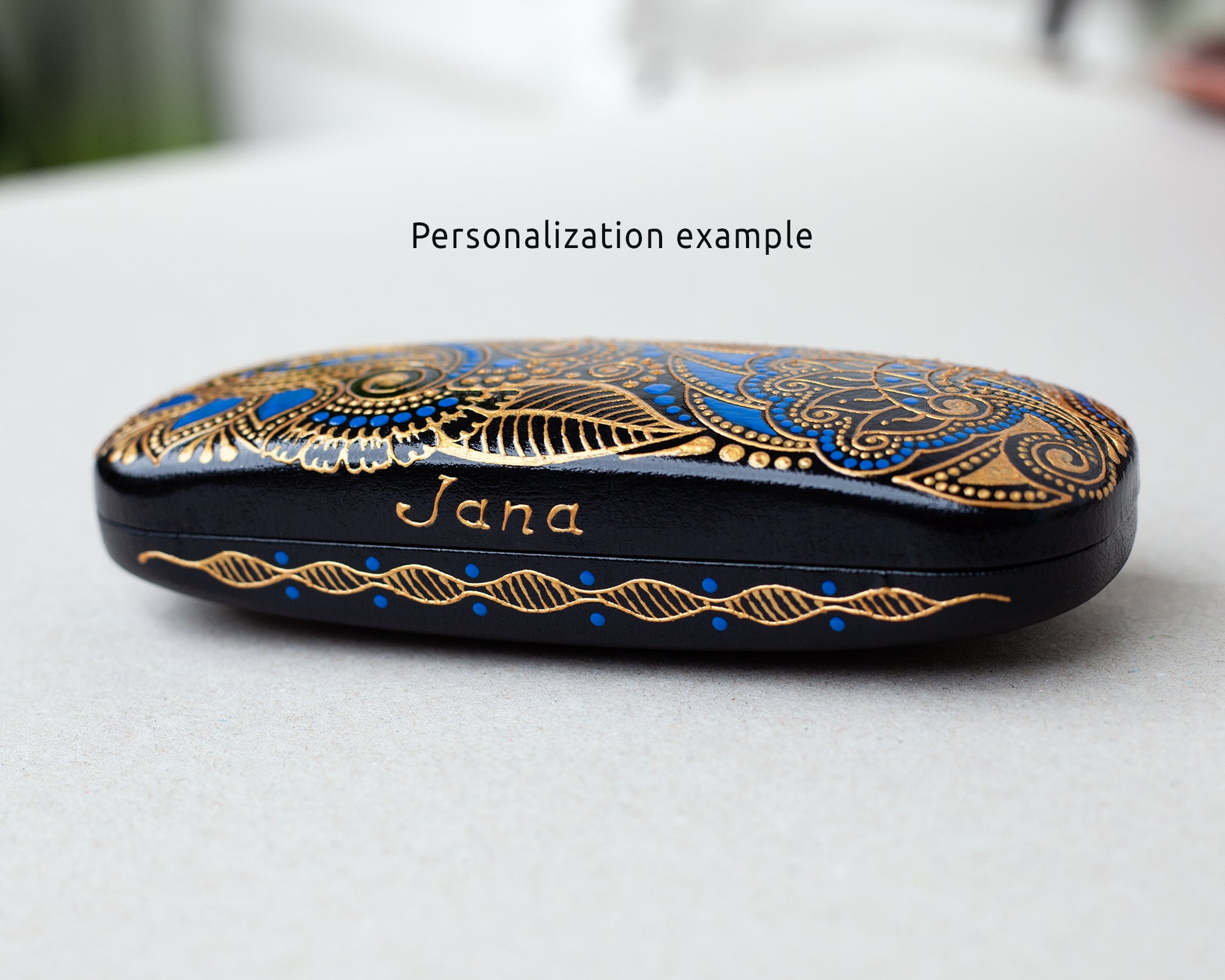 Eyeglasses case, hand-painted with blue and gold. Example of personalization with the name painted on the front of the case. Close-up view from the side.