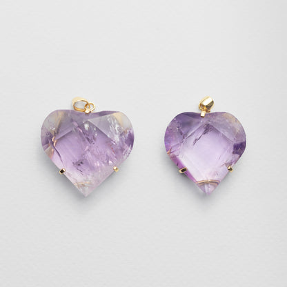 Two heart-shaped amethyst pendants with gold bail loops, displayed side-by-side on a light gray background.