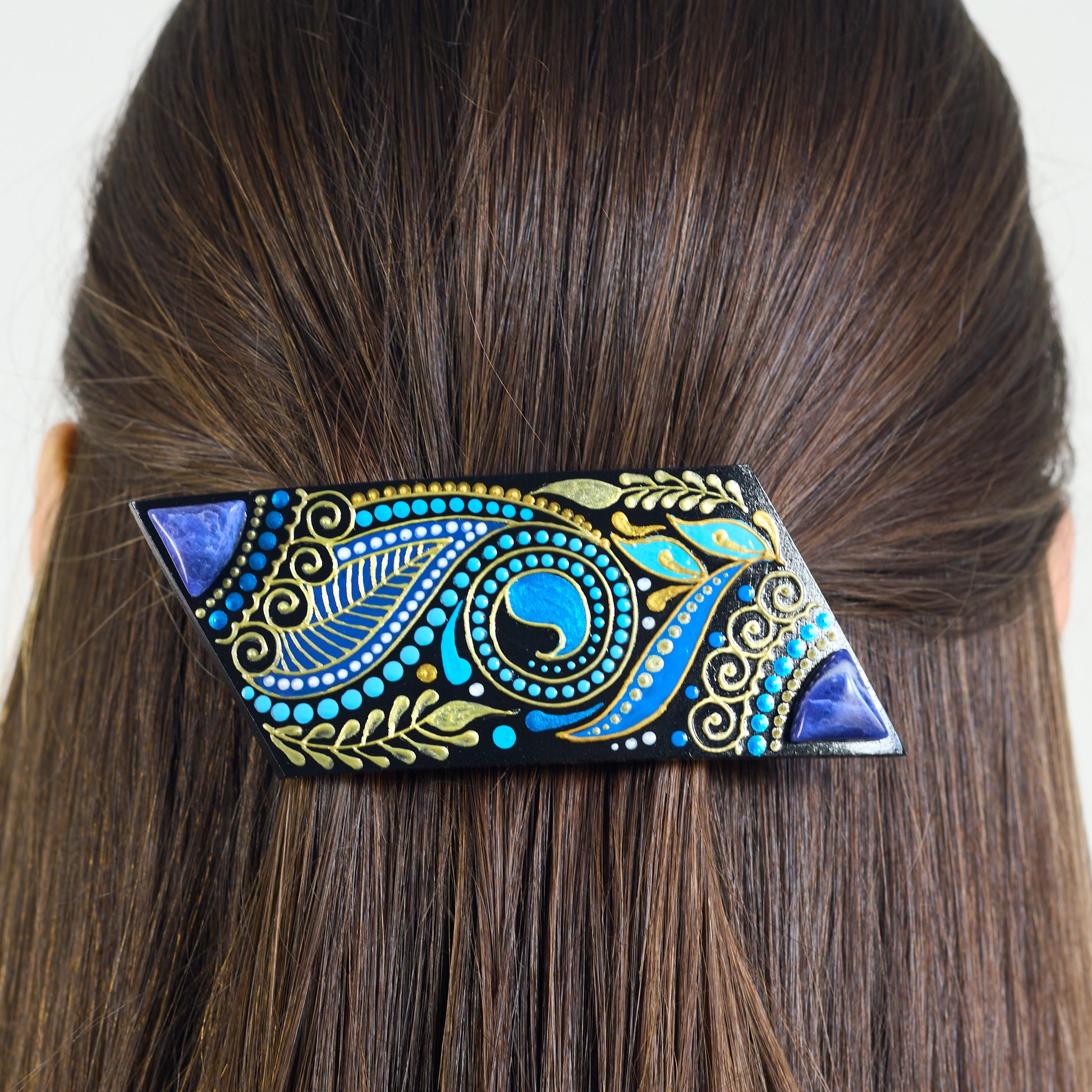 Decorative hair clip with blue and gold patterns on brown hair against a white background