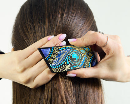 A woman fastens a hair clip hand-painted with blue design at the back of her dark hair.