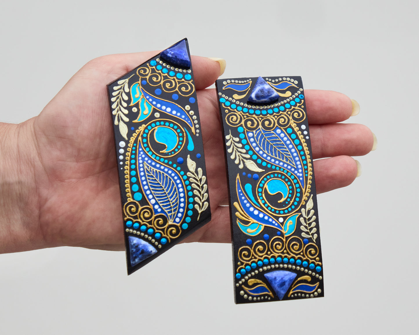 Hand holding two wooden hair barrettes painted in blue