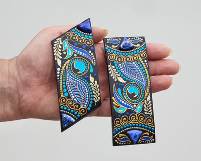 Hand holding two wooden hair barrettes painted in blue