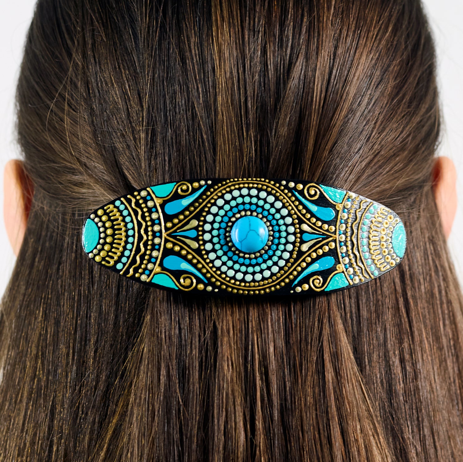 Close-up of dark hair with a colorful hand-painted wooden barrette clipped in, turquoise blue design.