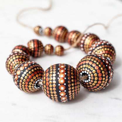 Wooden round beads collected in a garland, close-up view. Hand-painted beads in african style, gold and copper colors.