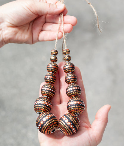 Wooden round beads collected in a garland, holding in hands. Hand-painted beads in african style, gold and copper colors.