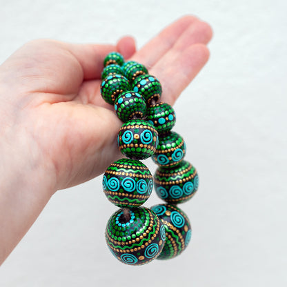 Green round beads collected in a garland, holding in a hand. Hand-painted wooden beads in african style, mint and gold colors.