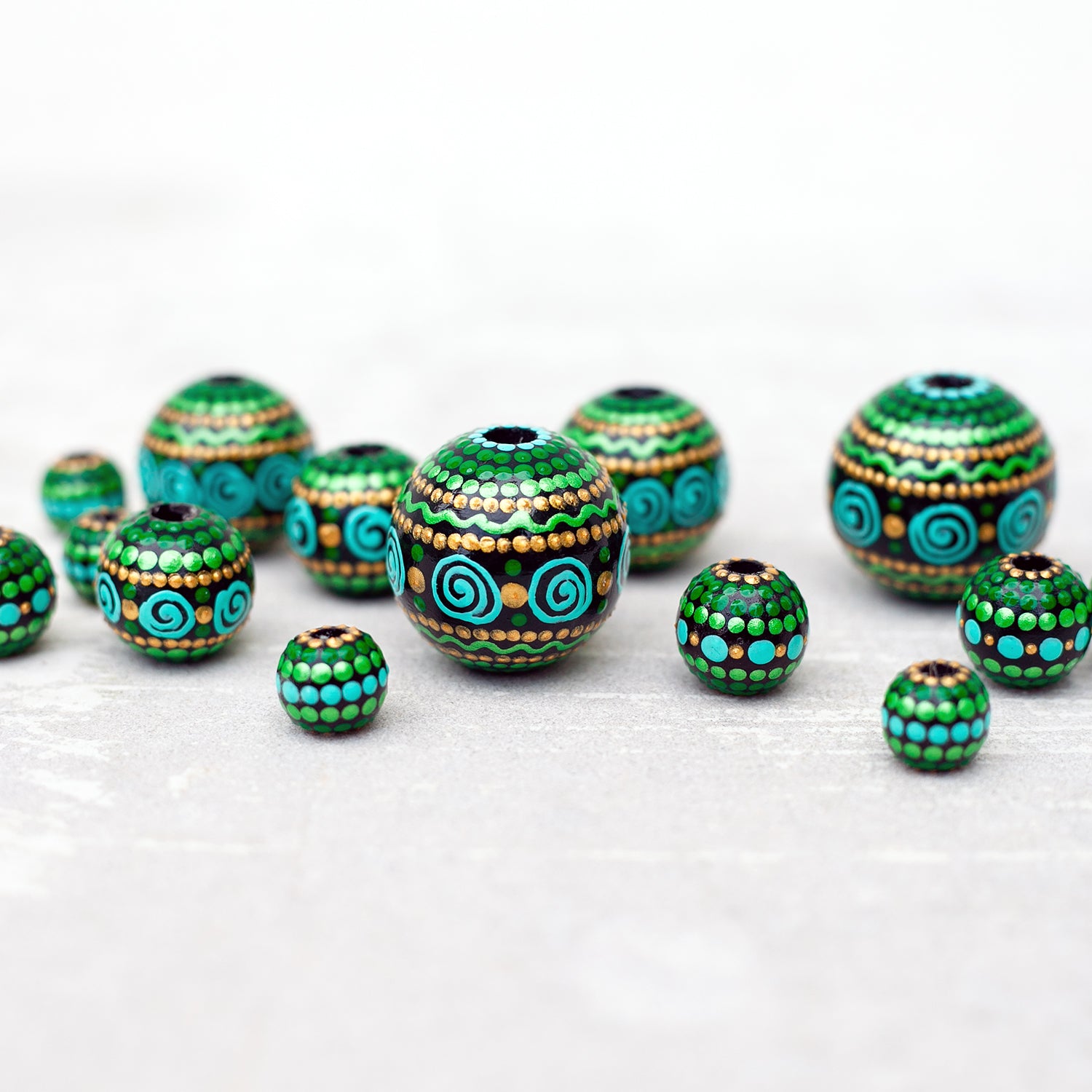 Large and small round  beads spread on the table, wooden hand-painted beads in african style. Green, mint and gold colors, close-up view