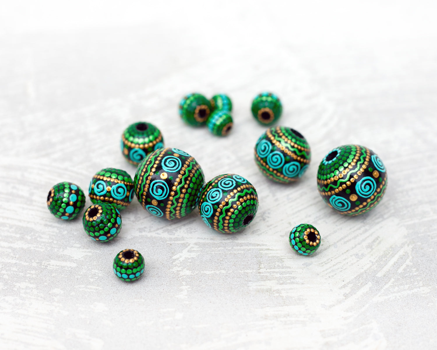 Large and small round  beads spread on the table, wooden hand-painted beads in african style. Green, mint and gold colors, close-up view