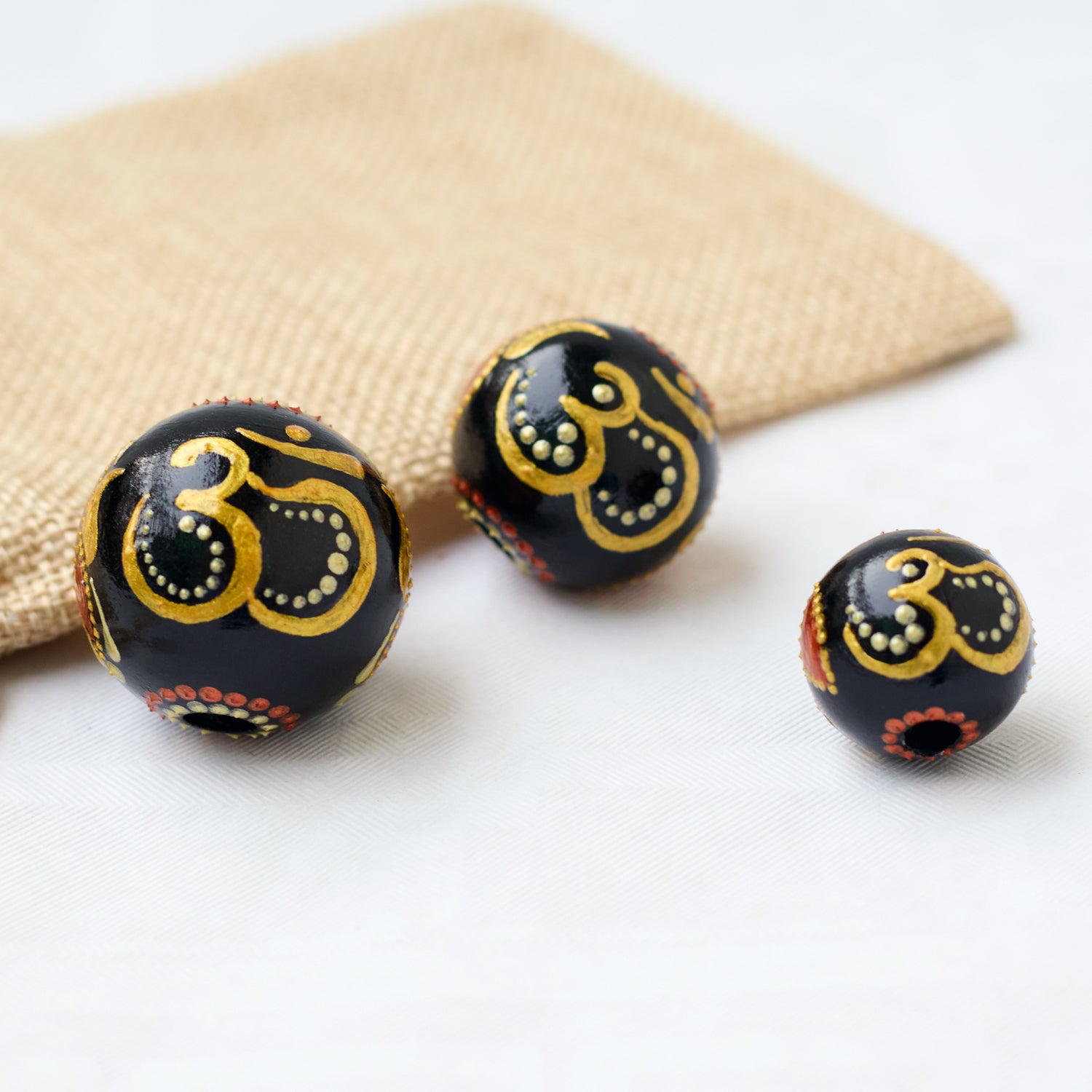 Three hand-painted wooden beads featuring the gold Om symbol on a white background. Close-up view
