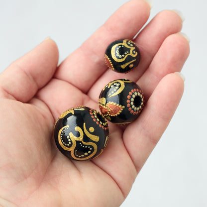 Wooden beads in a hand, three different sizes. Hand-painted large beads with the Om symbol.