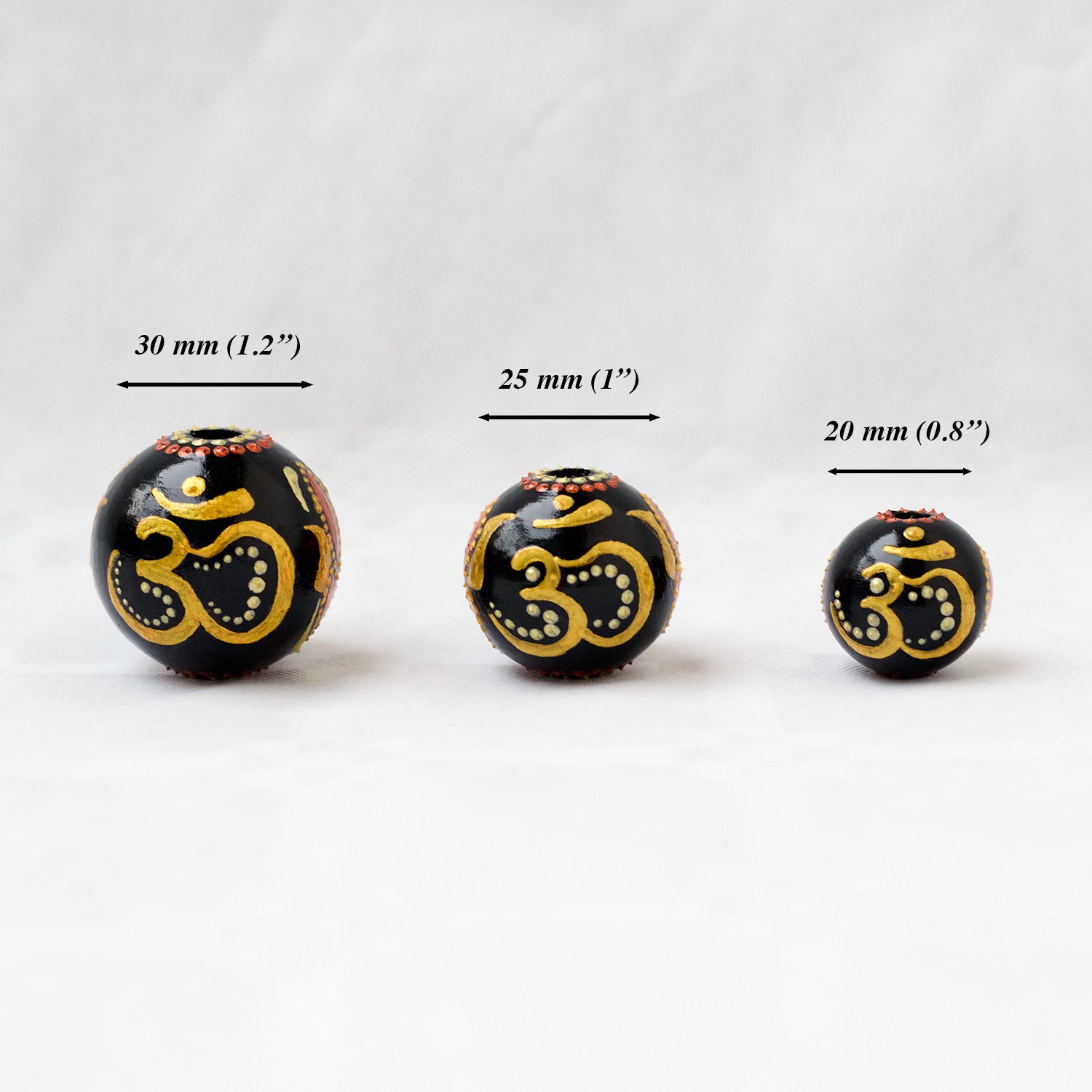 Wooden round beads in a row to show different sizes. Hand-painted large beads with the Om symbol.