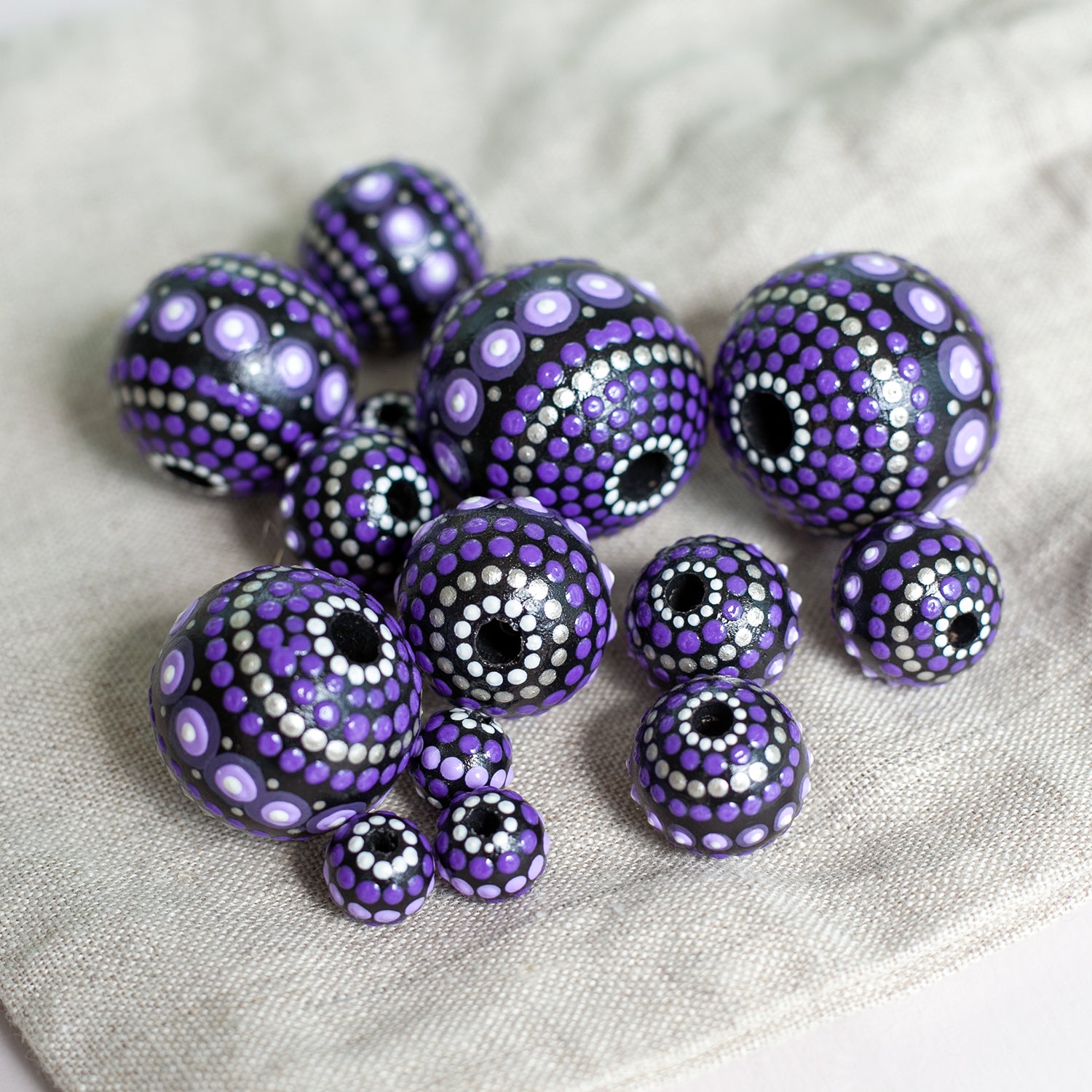 Large and small purple beads spread on a table, wooden hand-painted beads dot art. Round beads, view from the top