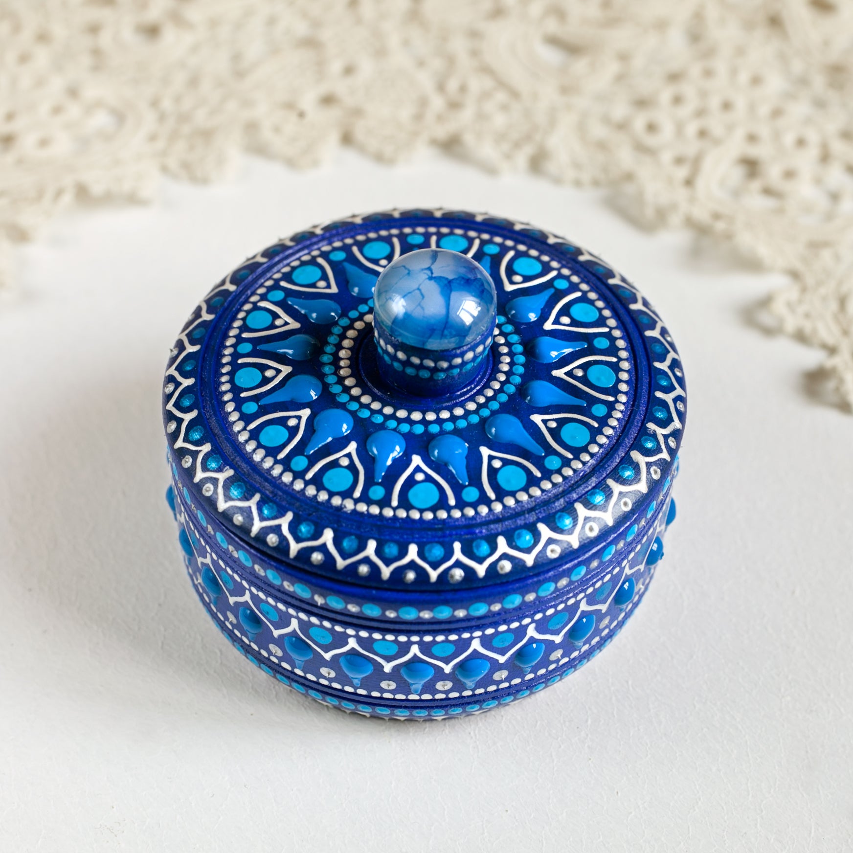 Wooden blue box with hand-painted design and blue agate stone on the lid. Standing on a white table