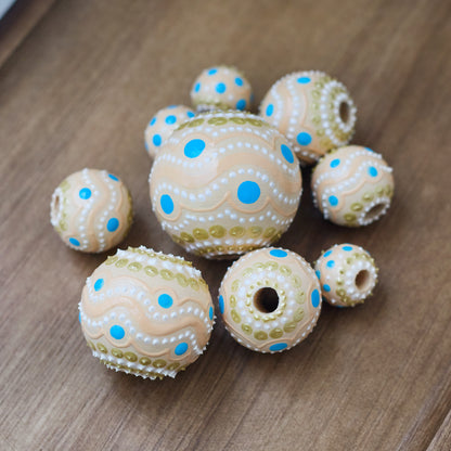 Large and small round  beads spread on wooden table, hand-painted beige boho beads, close-up view