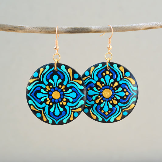 Pair of colorful mandala earrings hanging on a branch against a gray background