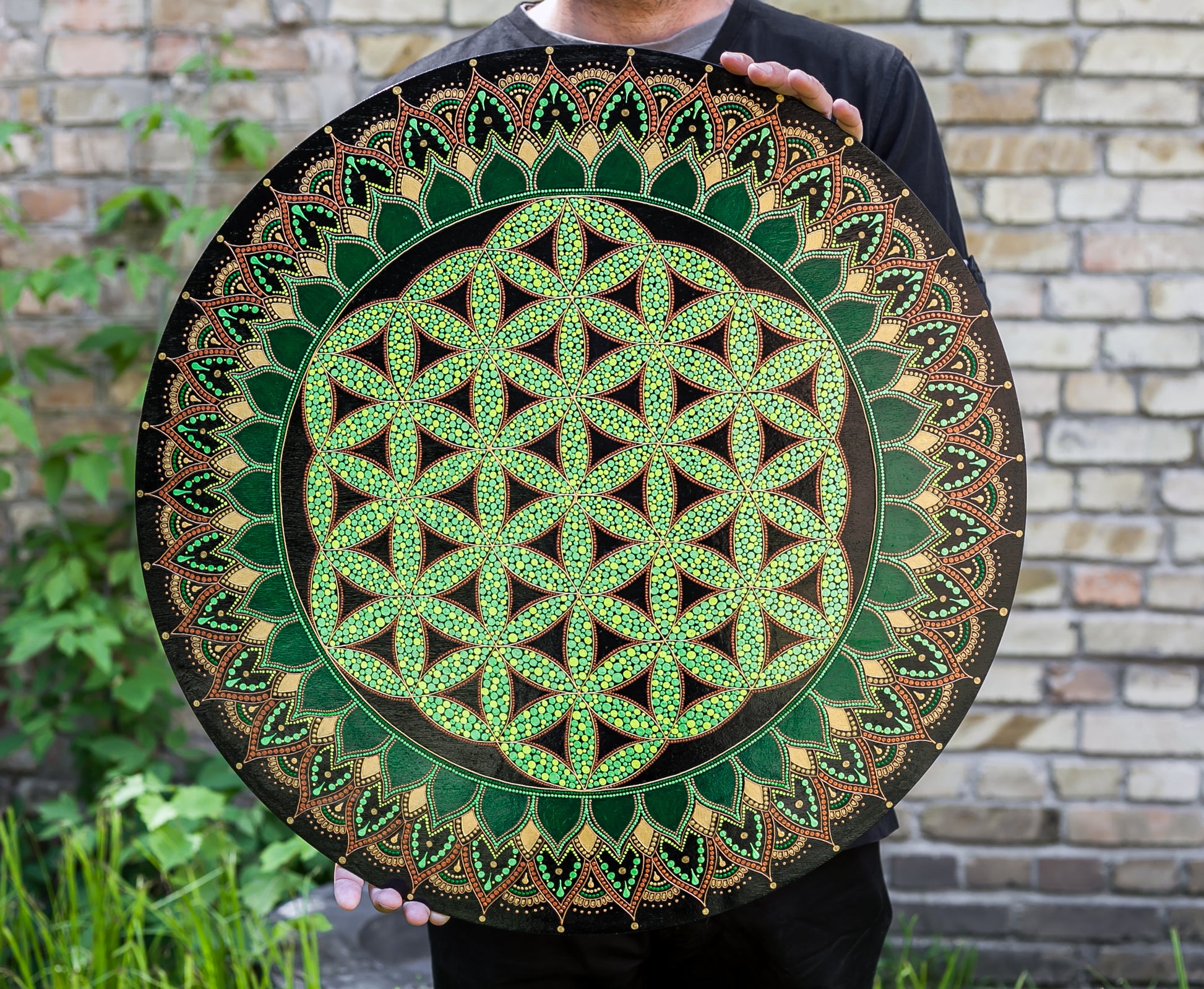 Flower of Life painted on a round canvas board, dot art technique, greencolors. Man holding the canvas in hands to show dimensions of 60 cm size