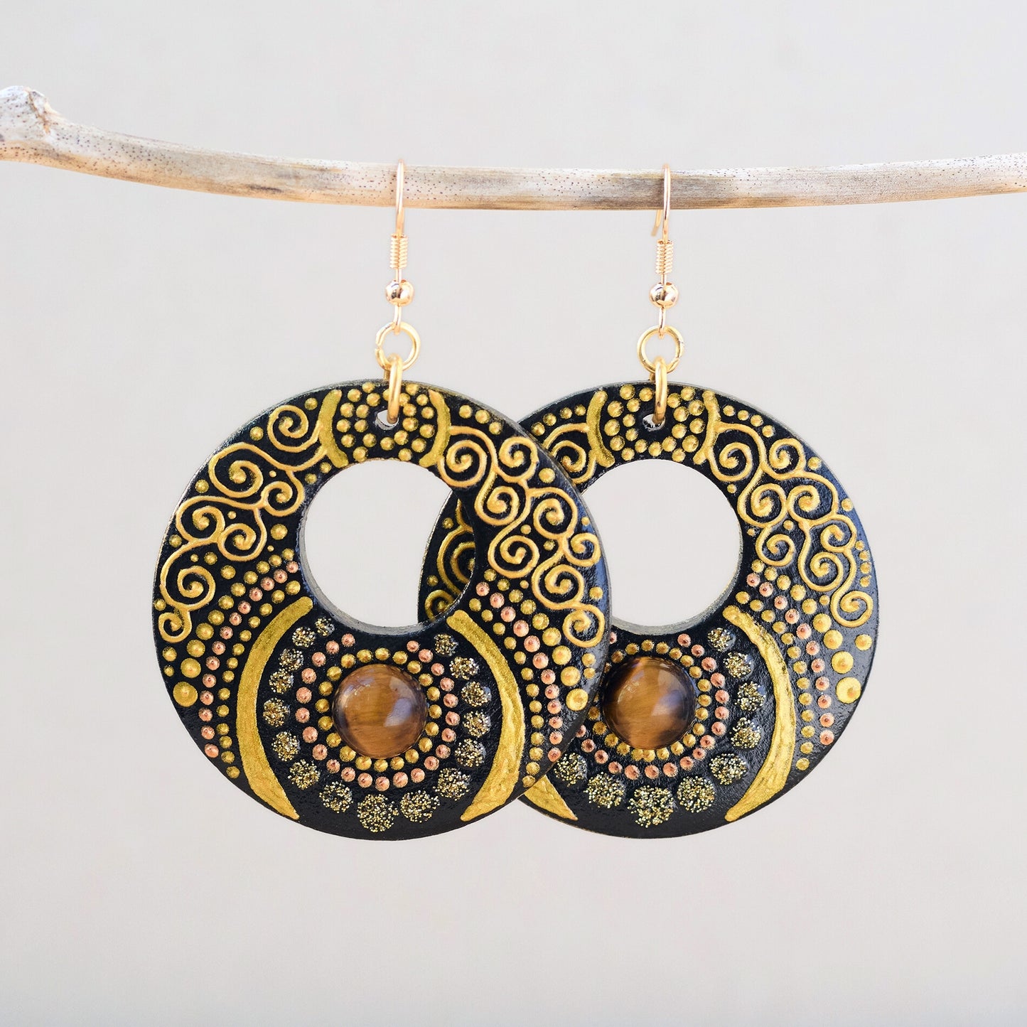 Wooden painted earrings with an inlaid Tiger Eye cabochon, decorated with fine golden swirls and textured dot motifs.