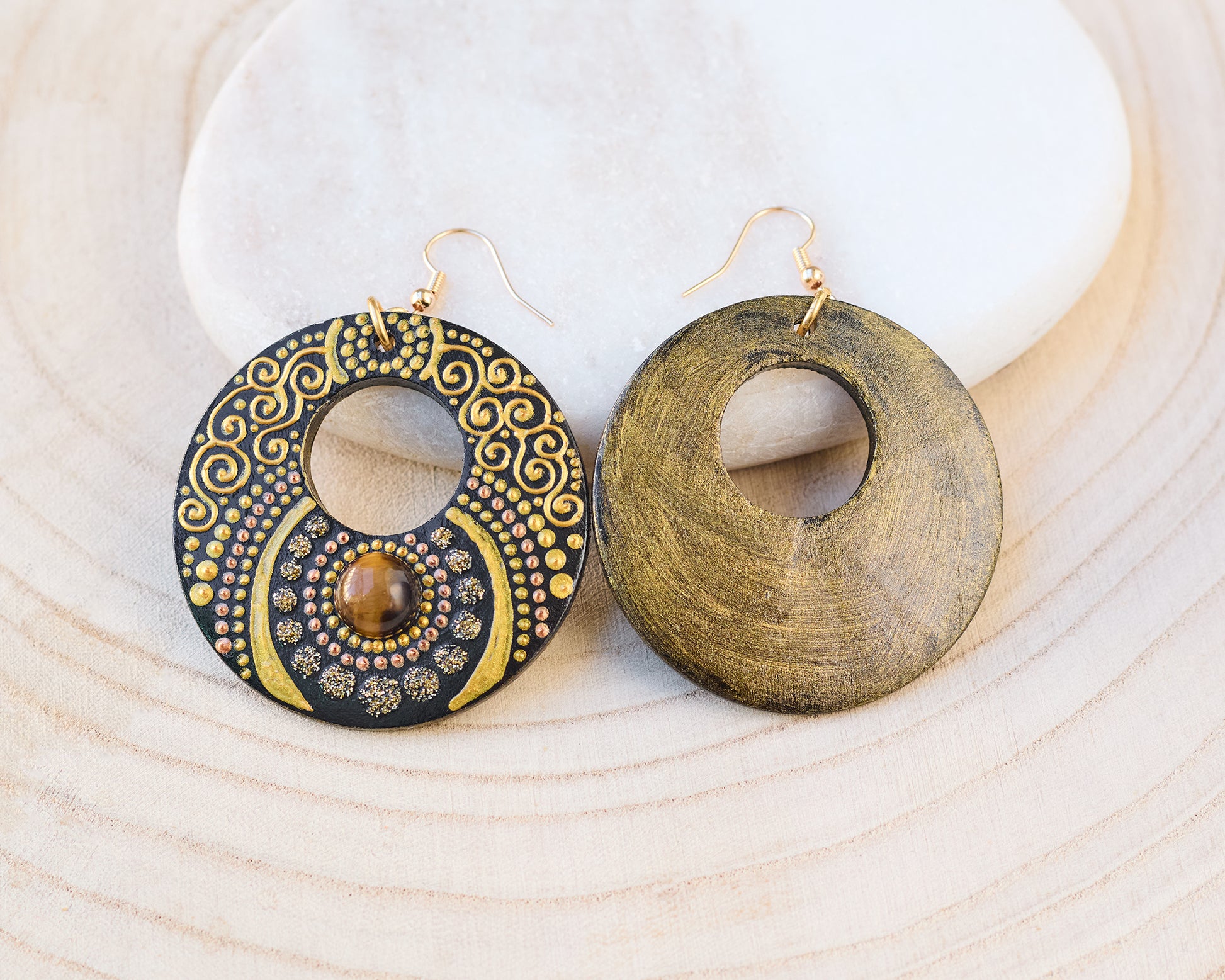 Wooden painted earrings with golden motif on a wooden background