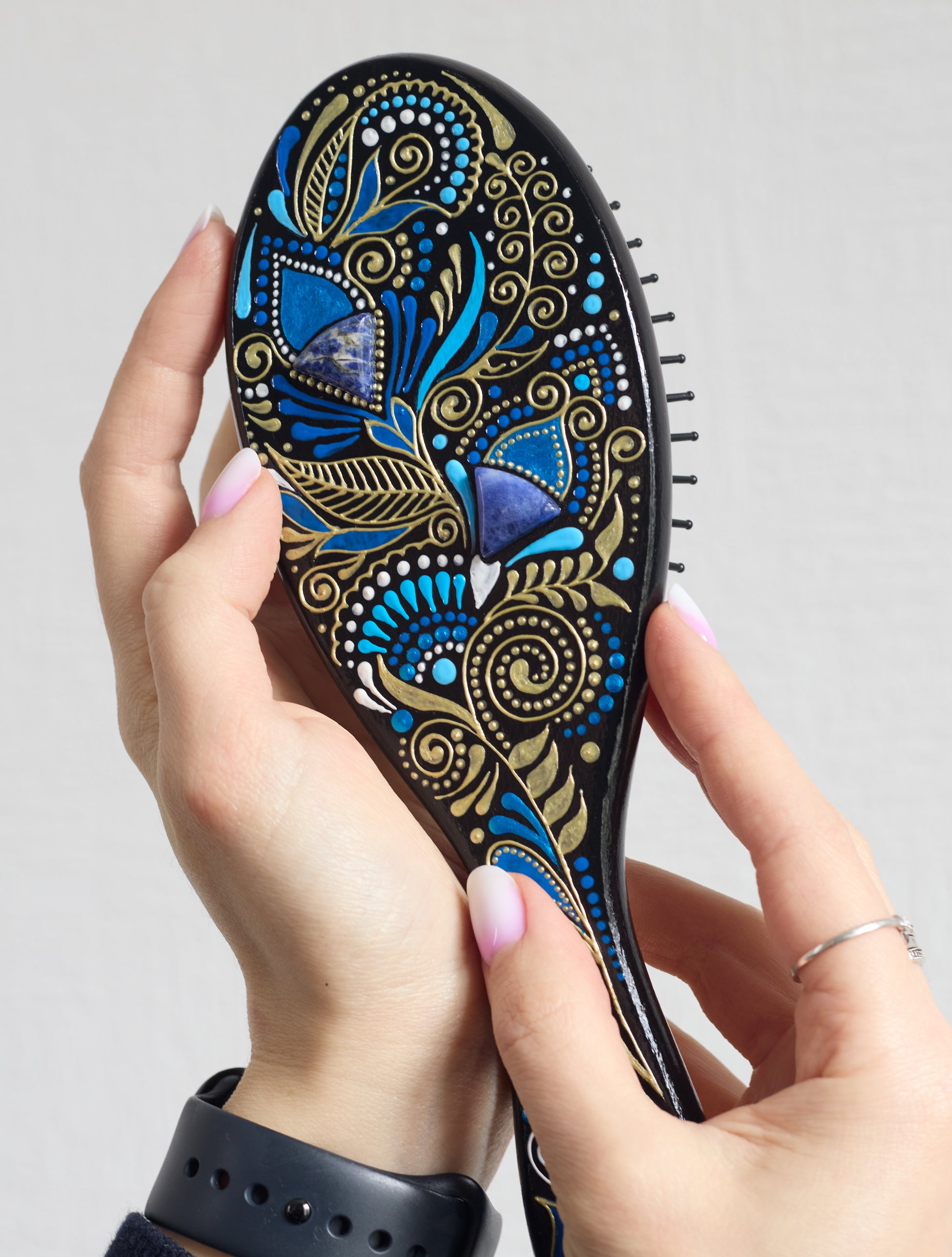 Hand holding a hand-painted wooden paddle hairbrush with blue floral  design.