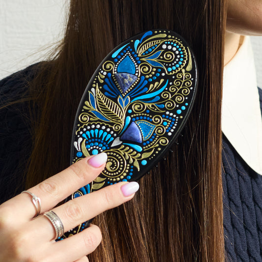Close-up of a hand brushing dark hair with a hand-painted wooden hairbrush, focusing on the brush in use.