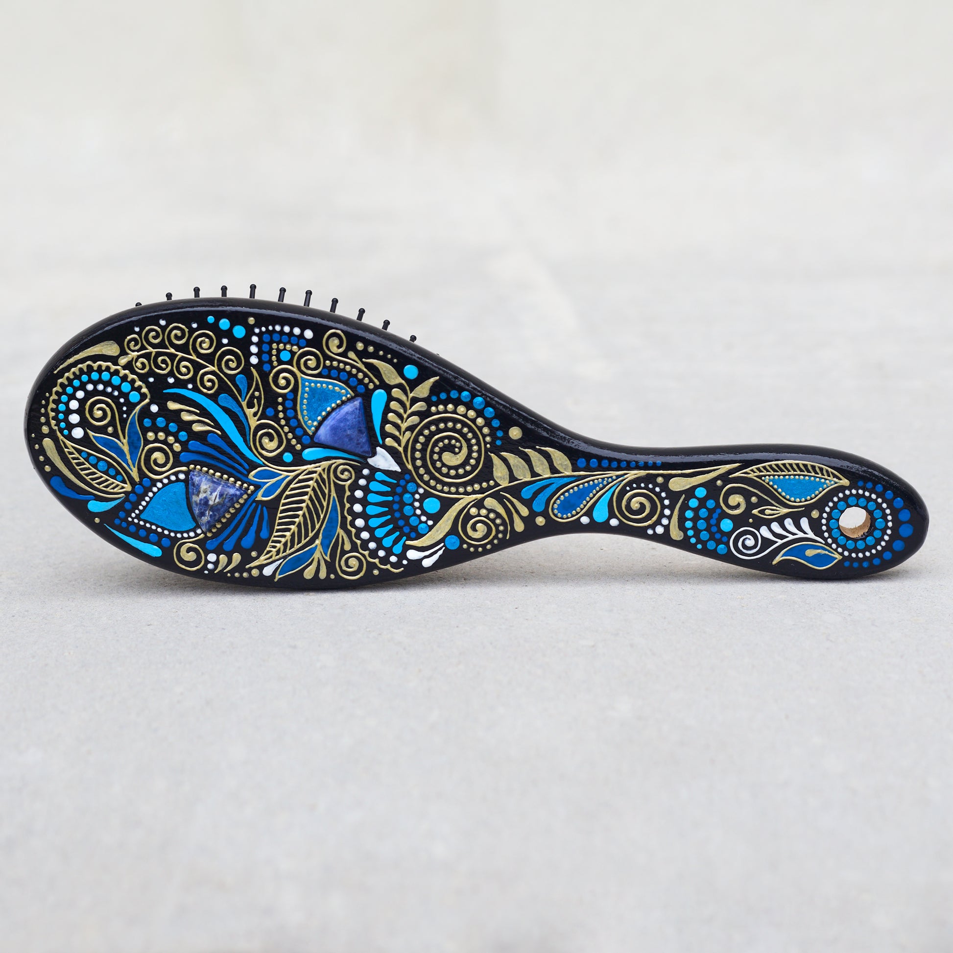 Wooden hairbrush with blue and gold patterns on a light gray background
