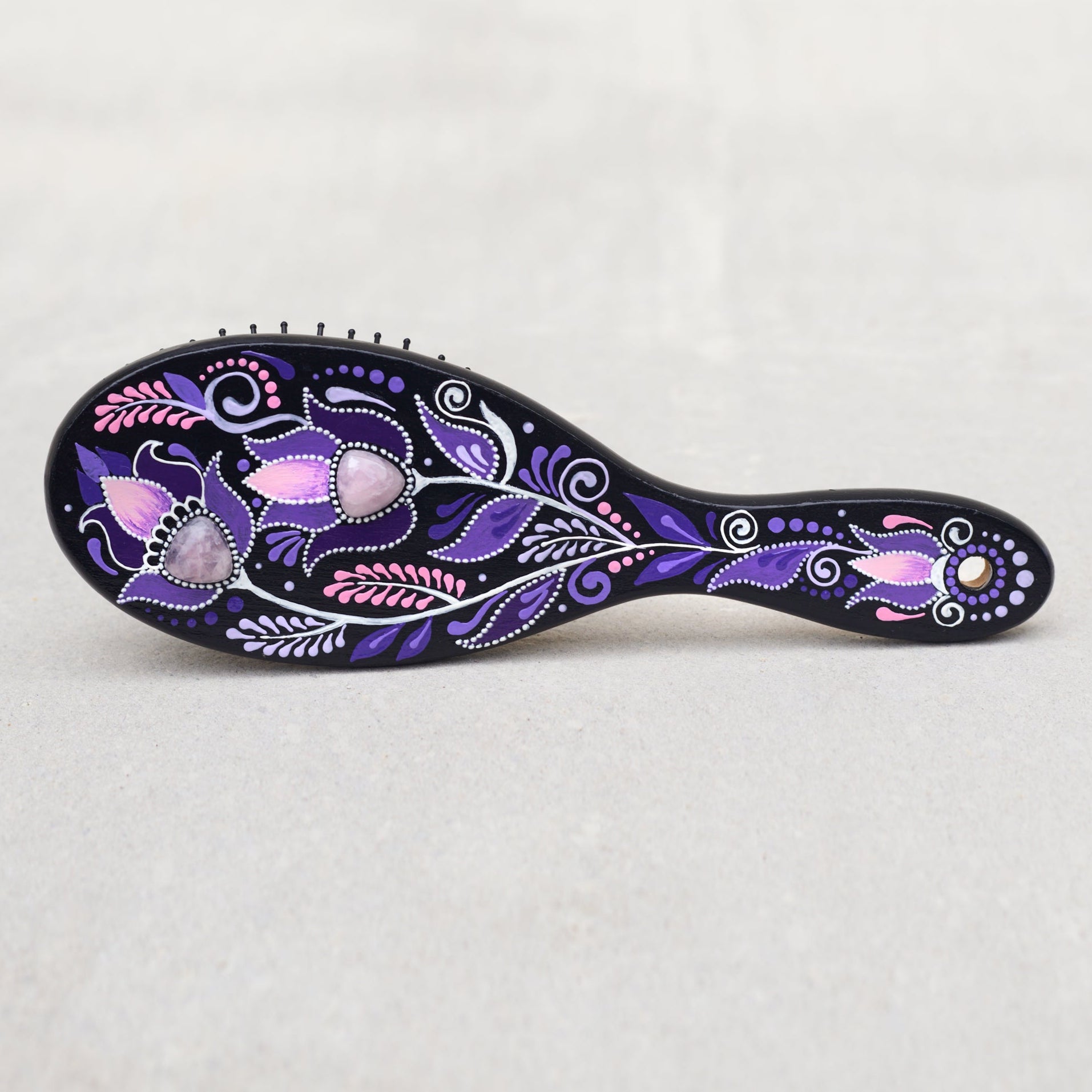 Wooden hand-painted hairbrush with purple and pink floral patterns on a light gray background