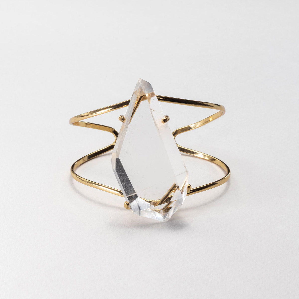 A gold wire ring featuring a large, clear, faceted crystal point, photographed on a clean white background.