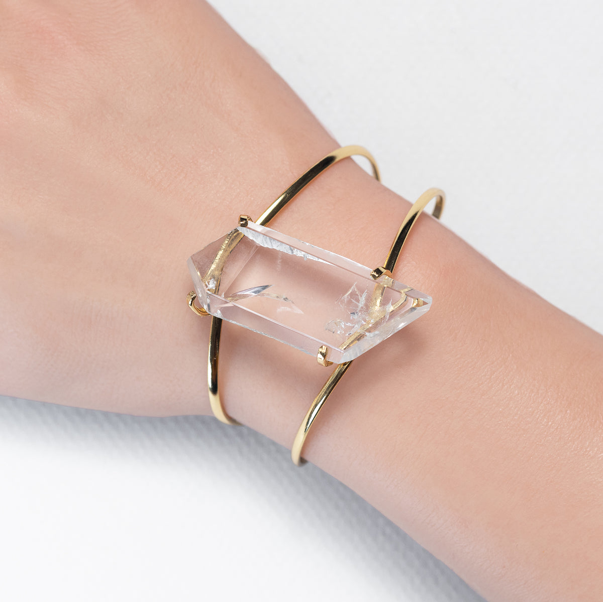 Gold bracelet with a clear crystal on a wrist against a light background