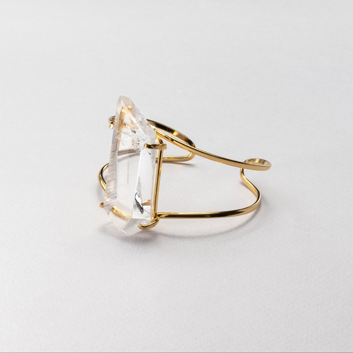 Gold bracelet with a clear gemstone on a light gray background