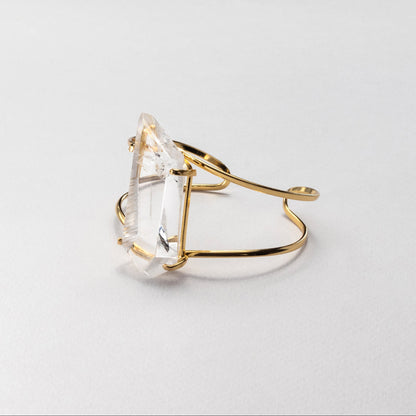 Gold bracelet with a clear gemstone on a light gray background