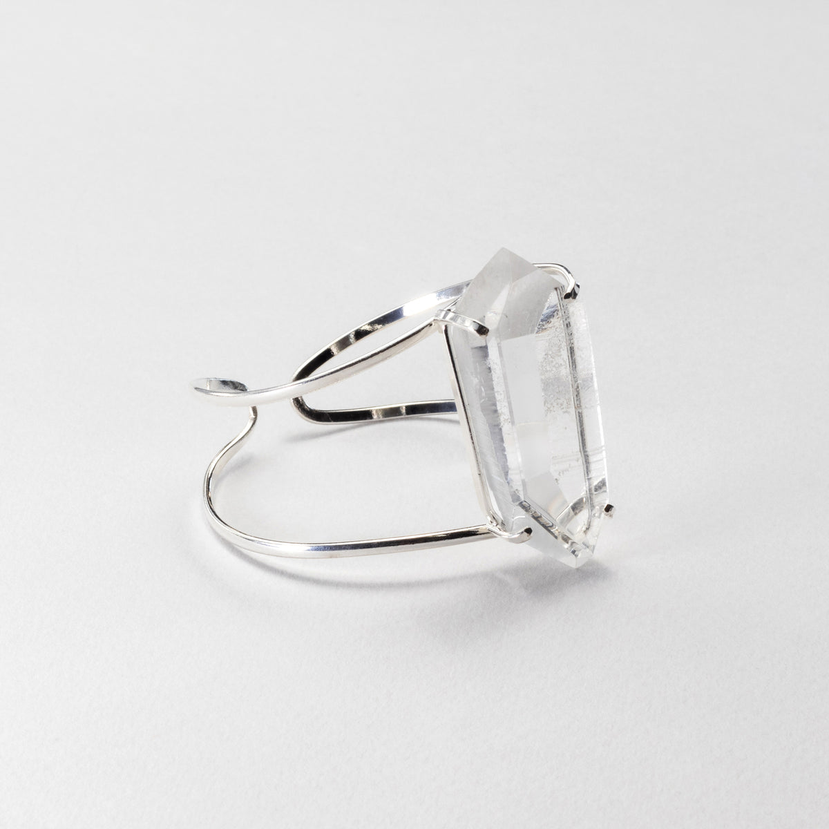 A silver-toned bracelet featuring a large, clear rectangular gemstone, photographed on a clean, light gray background.