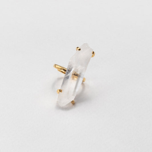 A gold ring featuring a raw, pointed clear quartz crystal, photographed on a clean white background.