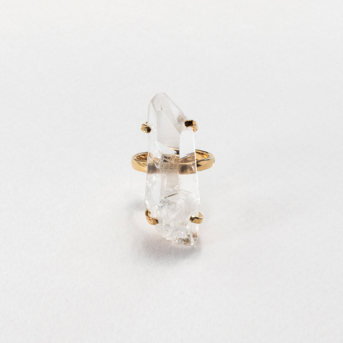 A gold ring featuring a raw, pointed clear quartz crystal, photographed on a clean white background.