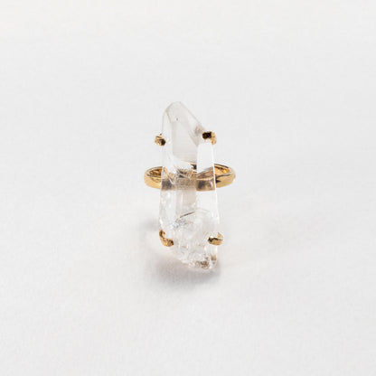 A gold ring featuring a raw, pointed clear quartz crystal, photographed on a clean white background.