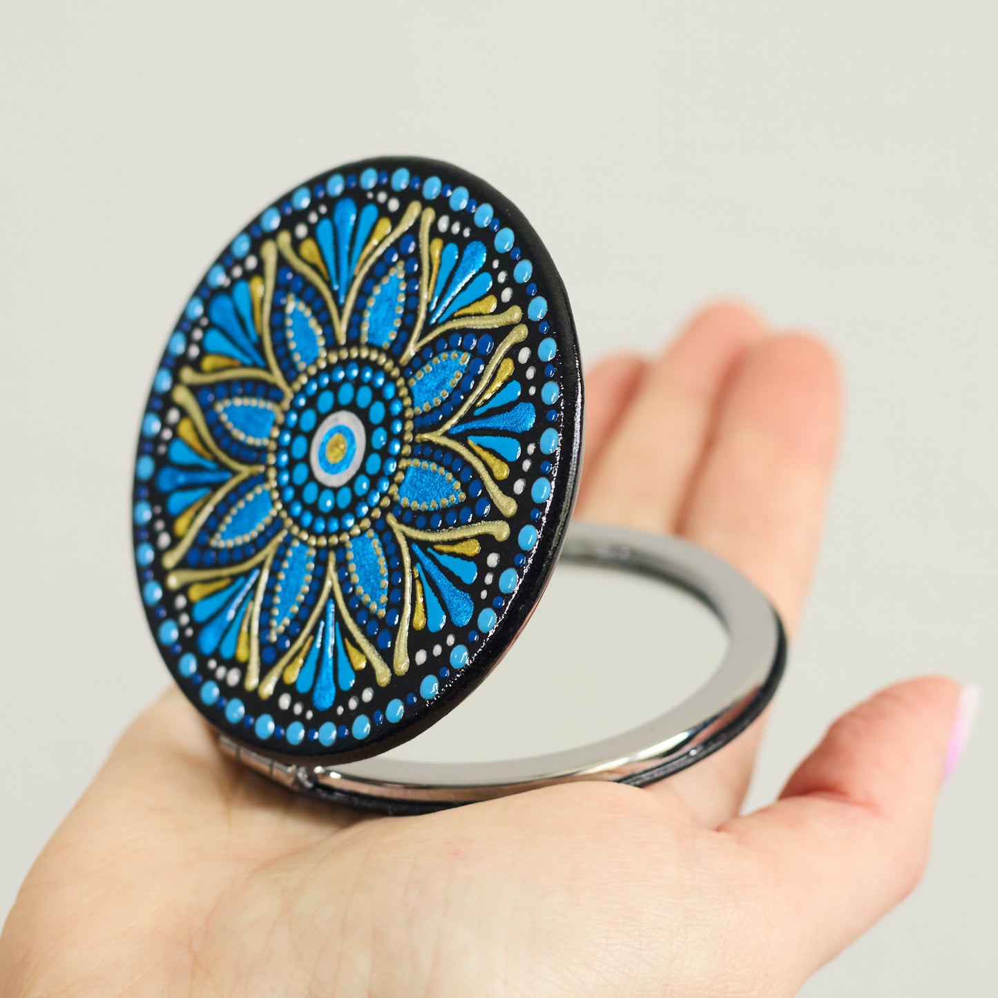 Compact mirror with blue mandala design held in a hand, round shape