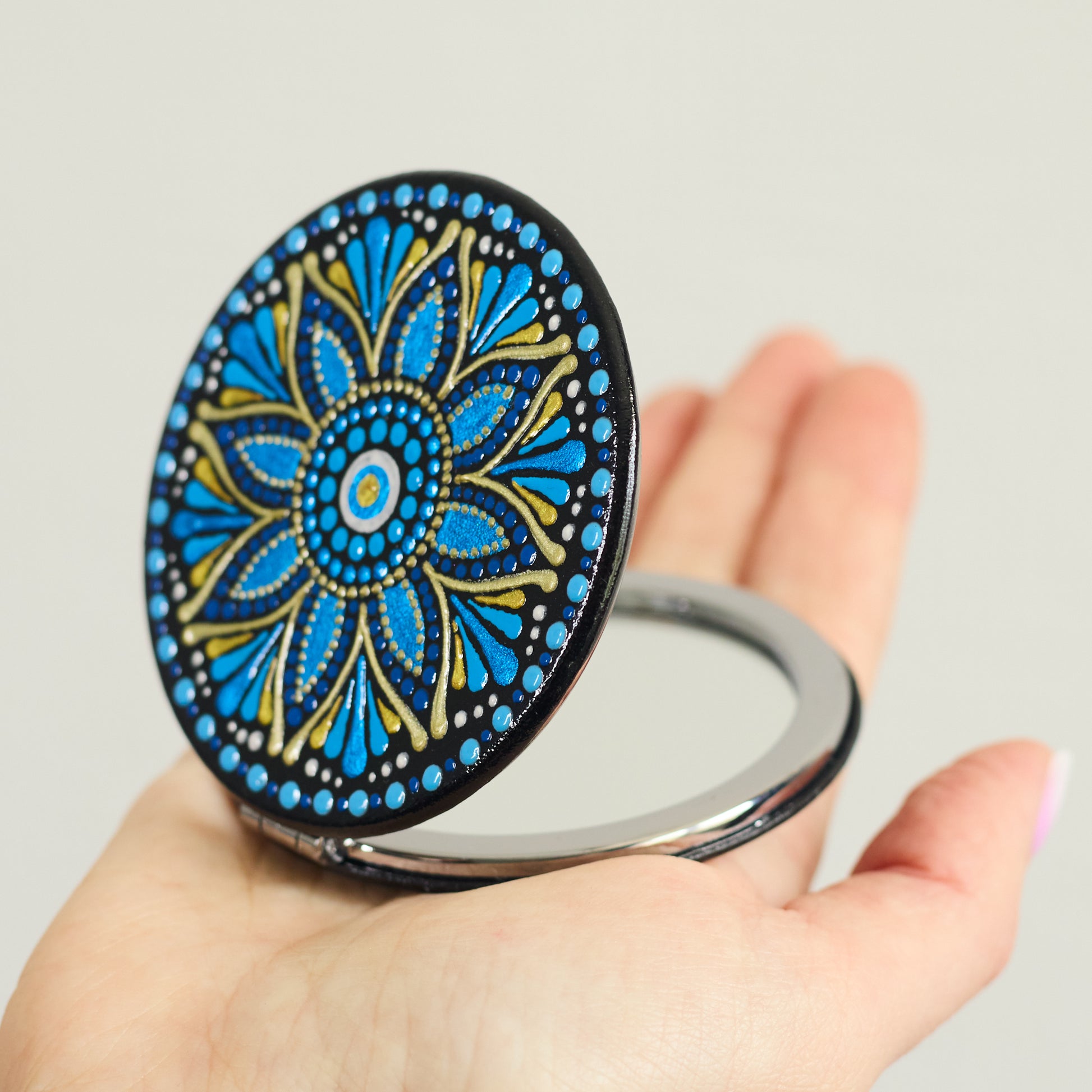 Compact mirror with blue mandala design held in a hand, round shape