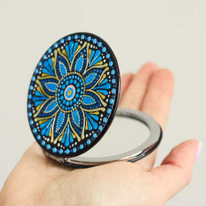 Compact mirror with blue mandala design held in a hand, round shape