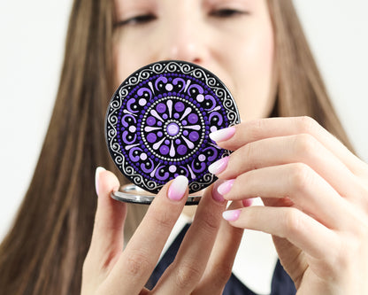 Woman looking in the compact mirror with purple mandala hand-painted design.