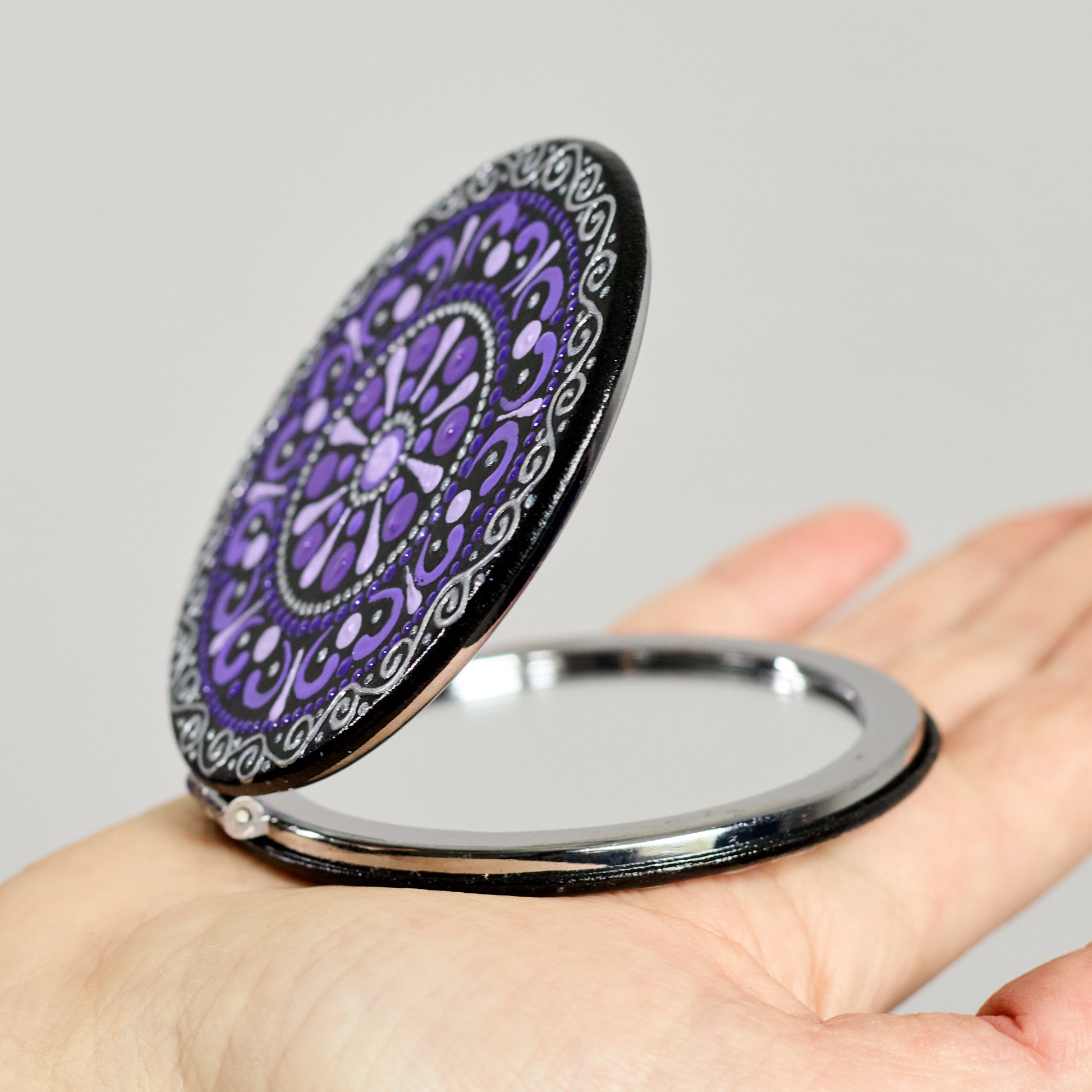 Compact mirror with purple mandala design held in a hand, round shape