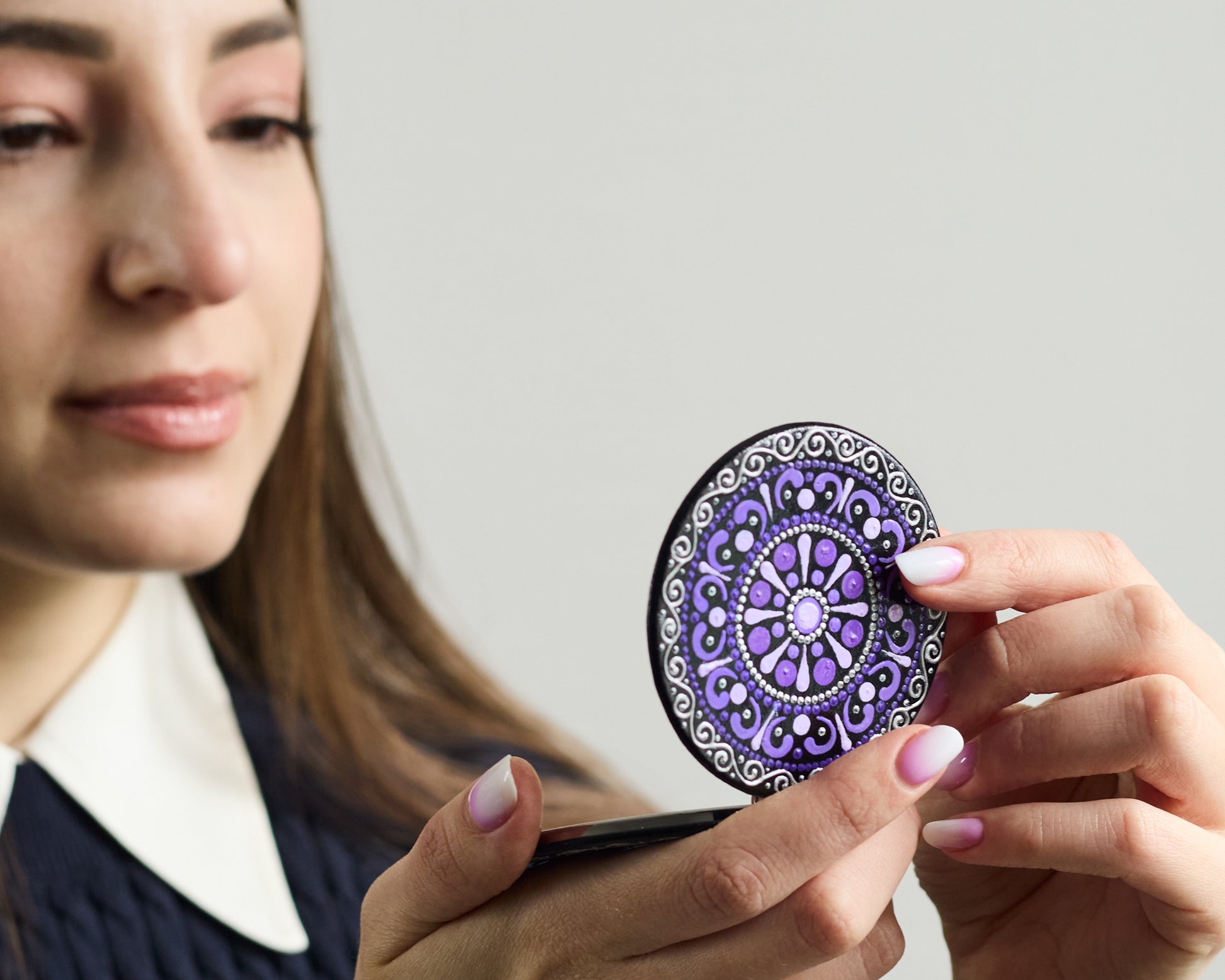 Woman looking in the compact mirror with purple mandala hand-painted design.