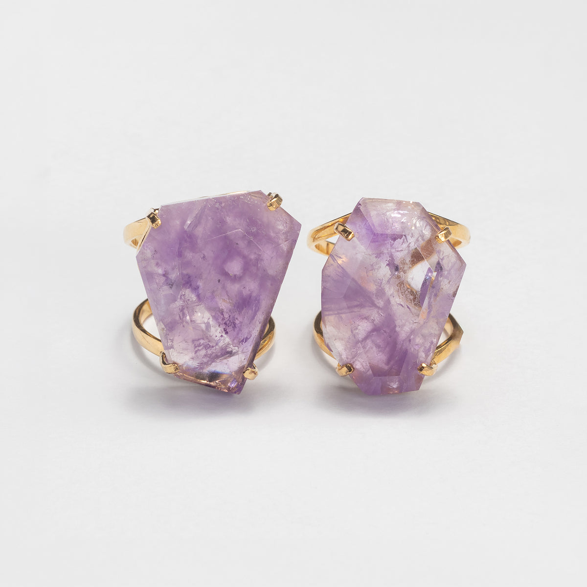 Two rings featuring large, irregular faceted purple amethyst gemstones in gold band, displayed on a clean white background.