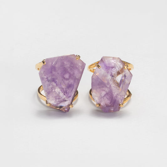 Two rings featuring large, irregular faceted purple amethyst gemstones in gold band, displayed on a clean white background.