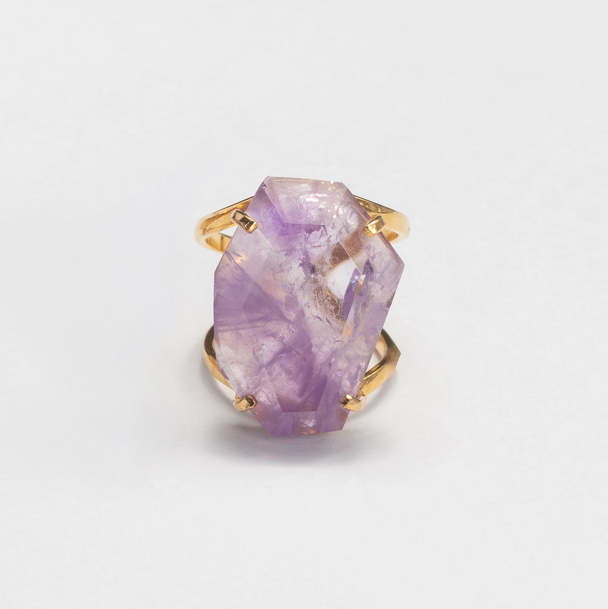 A gold ring featuring a large, faceted purple crystal gemstone, photographed on a clean white background.