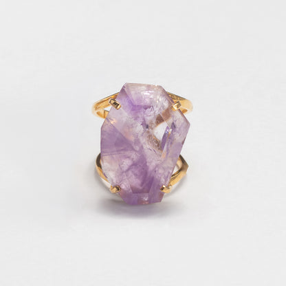 A gold ring featuring a large, faceted purple crystal gemstone, photographed on a clean white background.