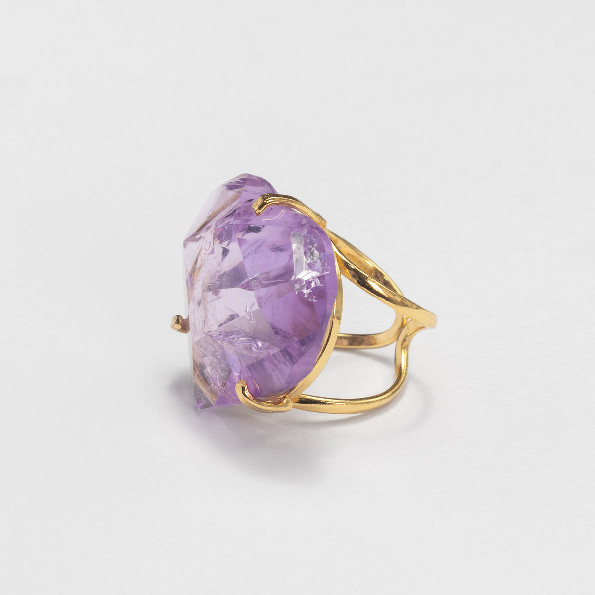 A gold ring featuring a large, irregularly shaped faceted purple gemstone, photographed on a clean white background.
