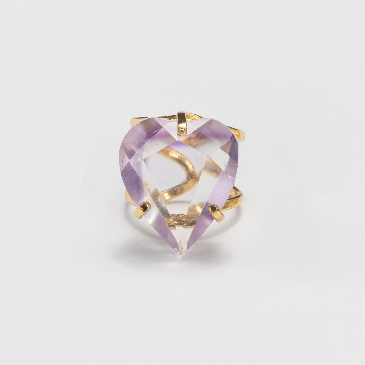 A heart-shaped clear gemstone ring with a gold band and prongs, showing a light purple/lavender reflection, photographed on a clean white background.
